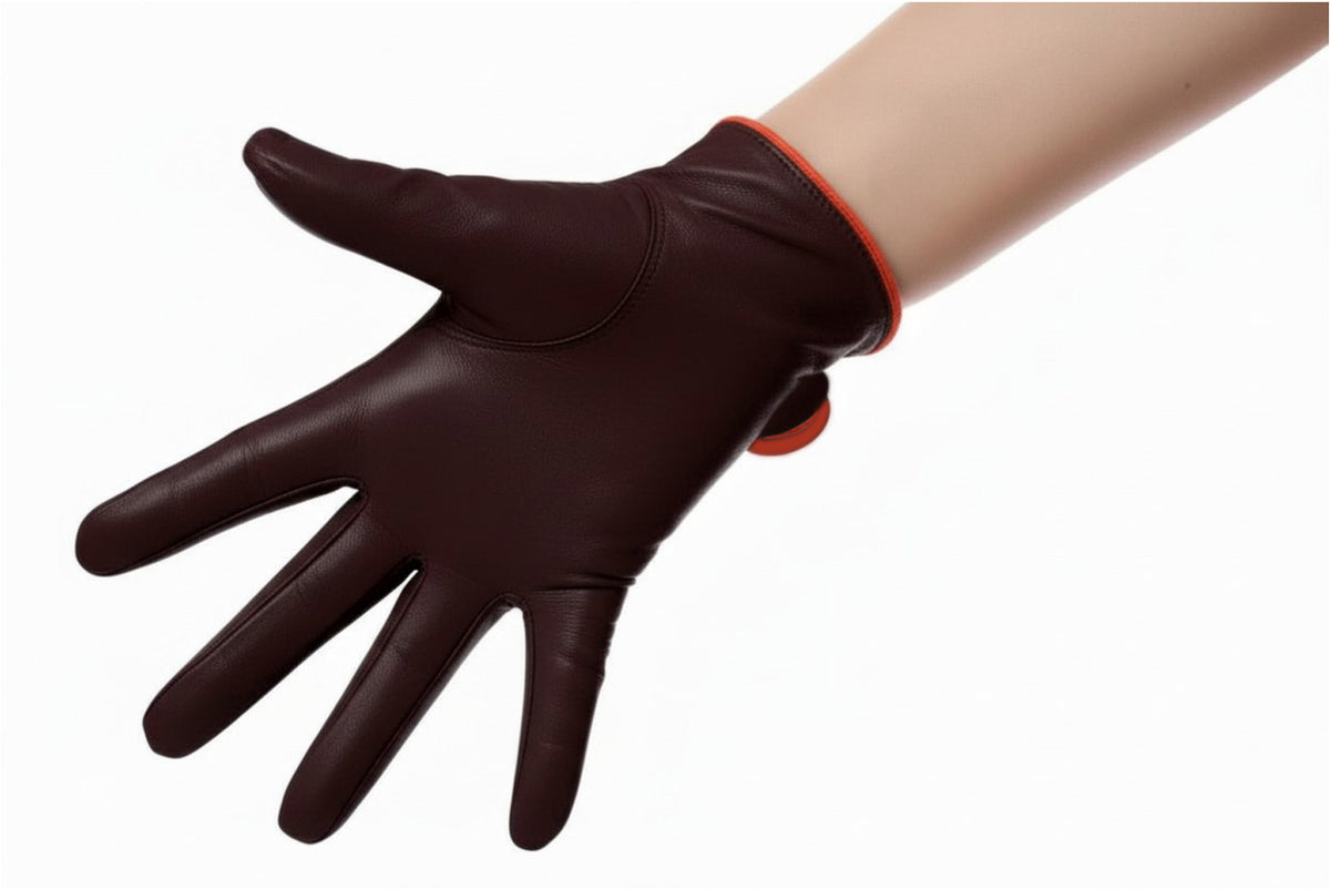 A deep dark brown leather glove with orange piping worn on a model's hand, showing the back of the hand isolated on a white background.